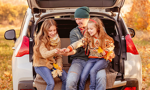 A man and two children are seated in the trunk of a car, smiling and enjoying their time together