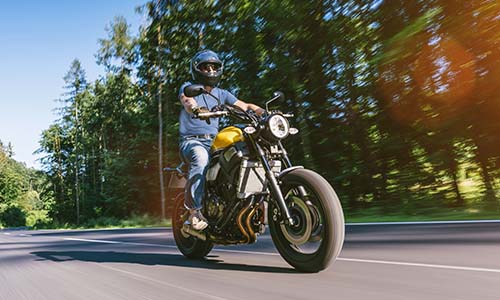 A man riding a motorcycle along a winding road surrounded by trees and greenery